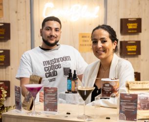 Deux exposants souriants présentant des boissons et produits bien-être sur un stand de salon