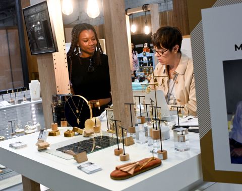 Deux personnes discutant devant un stand de bijoux modernes, avec des pièces exposées sur le comptoir.