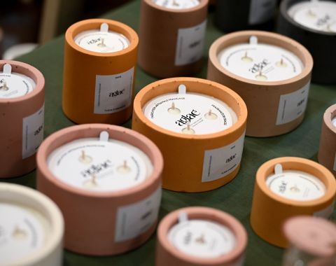 Bougies parfumées artisanales dans des contenants en béton coloré, présentées sur un stand lors d'un salon.