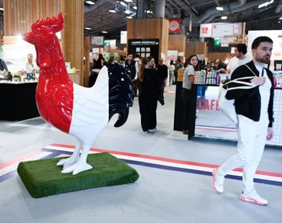 Statue de coq géante en installation, avec des visiteurs observant l’œuvre lors d’un événement.