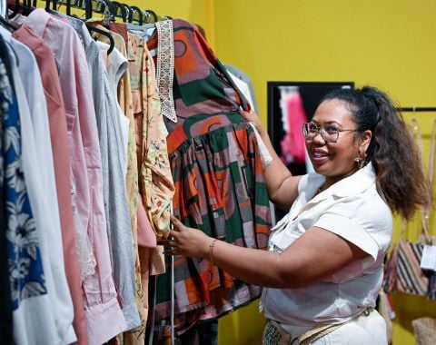 Femme souriante choisissant une robe dans un étalage de vêtements colorés sur un marché.