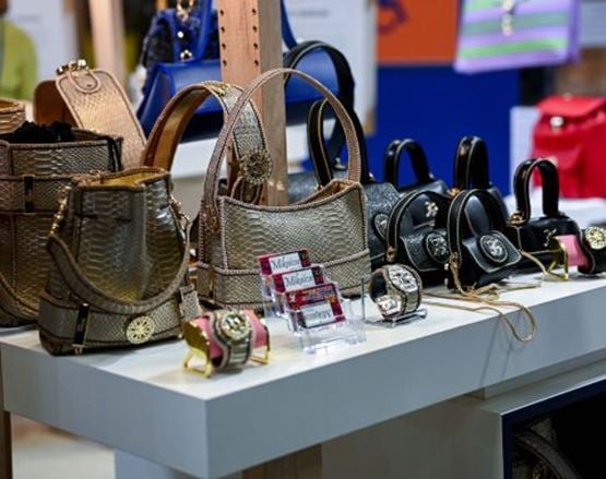 Exposition de sacs à main en cuir, avec des modèles dorés, noirs et rouges, accompagnés de montres et accessoires sur un comptoir.