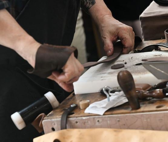 Artisan travaillant le cuir à la main sur un établi, découpant une lanière avec des outils traditionnels.