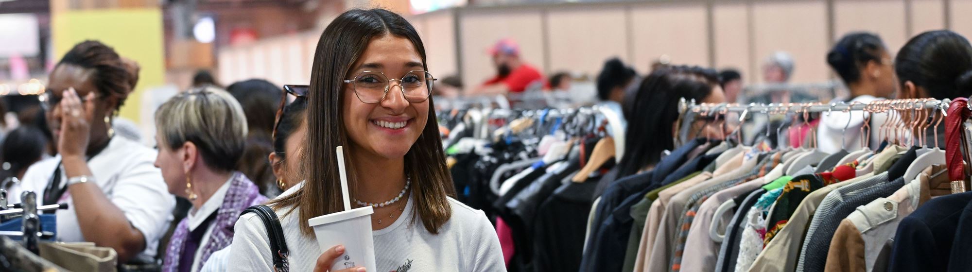 femme souriante devant des portants de vetements de seconde main
