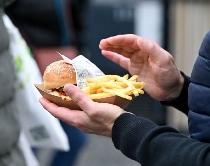 Homme tenant une barquette de frites et un burger dans la main