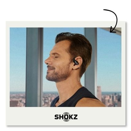 Homme portant des écouteurs sans fil Shokz à conduction osseuse, de profil devant une fenêtre avec vue urbaine
