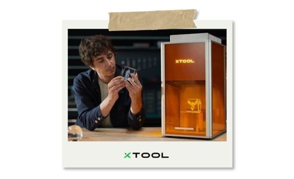 Homme manipulant une pièce transparente devant une machine de gravure laser xTool, dans un atelier moderne et technologique