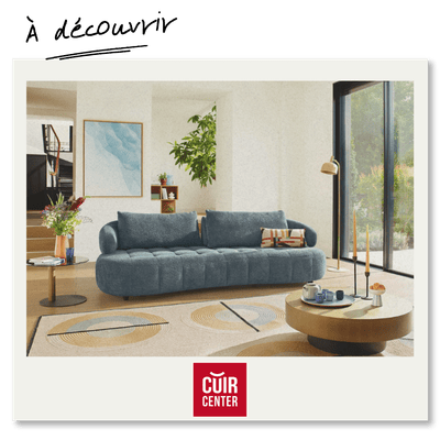 Image d'un canapé moderne en tissu, avec des coussins sur un tapis clair dans un salon lumineux. Un espace intérieur confortable et élégant, avec des fenêtres laissant entrer la lumière naturelle. Logo Cuir Center visible.