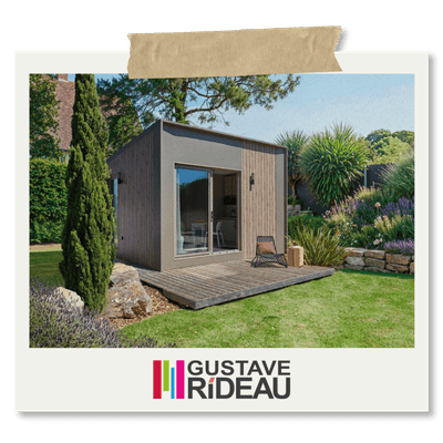 Image d'un studio de jardin en bois moderne, avec une terrasse en bois et des plantes luxuriantes autour. La photo montre un espace extérieur aménagé, avec un salon de jardin. Logo Gustave Rideau en bas