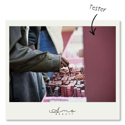 Une personne testant des produits de beauté, en particulier des rouges à lèvres, sur un stand de la marque AMS Beauty.