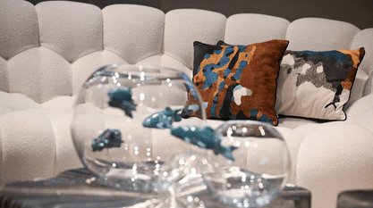 L'image montre un canapé blanc au design élégant, avec des coussins décoratifs aux motifs colorés et des objets en verre, créant une ambiance sophistiquée et moderne.