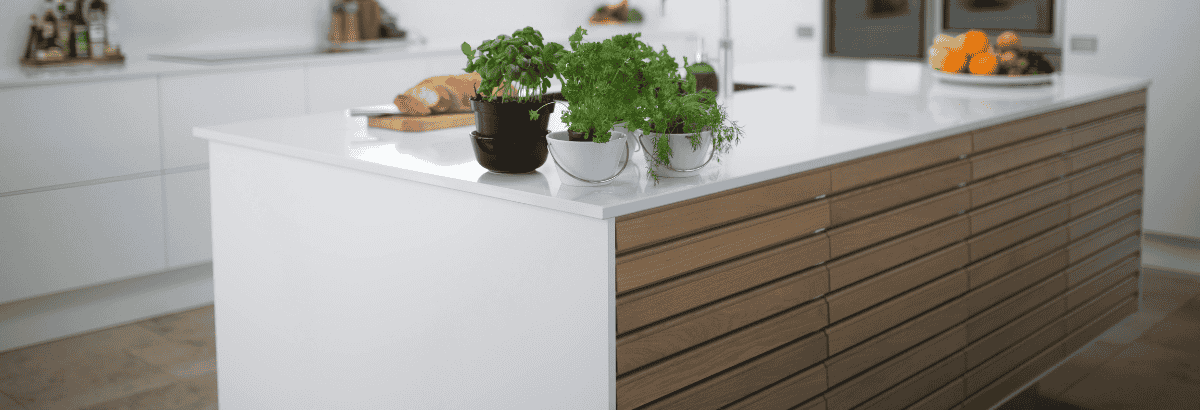 Ilot de cuisine blanc avec facades en bois et plantes aromatiques en pot.