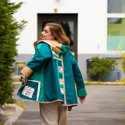 Femme portant une veste verte avec détails patchwork marchant devant une maison moderne.