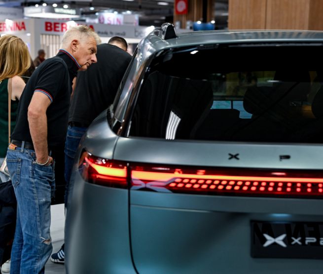 Deux visiteurs examinant l'arrière d'un véhicule électrique exposé lors d'un salon automobile, avec un modèle Xpeng