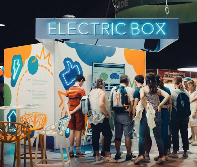 Visiteurs interagissant avec un stand "Electric Box" dans un salon, découvrant des informations interactives sur l'énergie et l'écologie