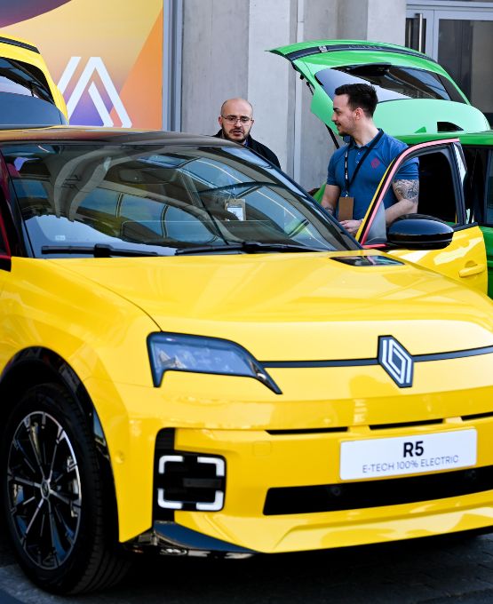 Deux personnes discutant autour d'une Renault R5 électrique, exposée lors d'un événement automobile, avec un modèle jaune et vert