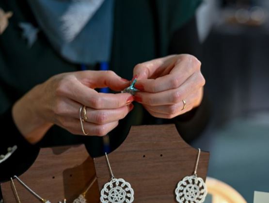 Mains d’une artisane assemblant une boucle d’oreille à la main sur un stand de bijoux artisanaux.