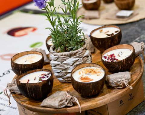 Bougies artisanales parfumées présentées dans des coquilles de noix de coco, disposées sur un plateau en bois.