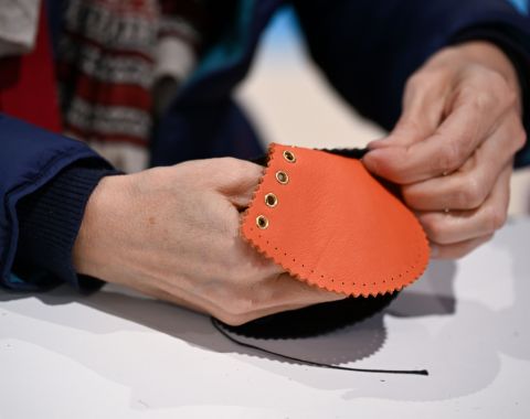 Mains assemblant une pièce en cuir orange avec des œillets métalliques lors d’un atelier artisanal.